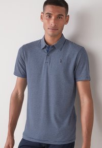 Polo de rayas en navy y blanco con cuello camisero, mangas cortas y un pequeño logo en el pecho; hecho de una tela ligera.