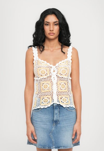 Hvid hæklede top med gule accenter, bølgede stropper, v-hals, knaplukning foran og blomsterkvadratmønstre. Matchet med en denim mini nederdel.