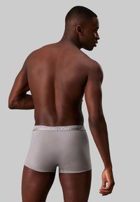 Sivi bokserice z mehkimi teksturami in elastičnim pasom z oznako "Calvin Klein," nosi model iz zadnjega kota.
