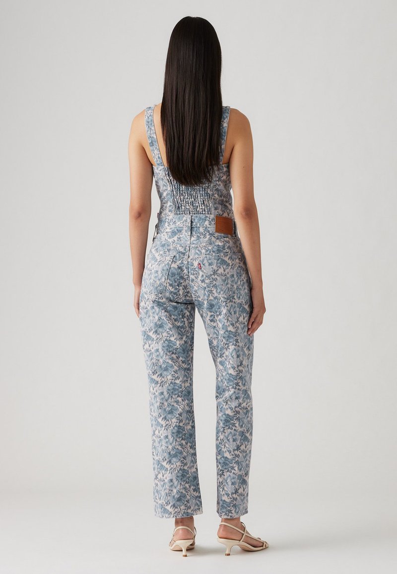 Salopette en denim à motif floral bleu avec un corsage ajusté, un dos smocké et une coupe droite. Patch en cuir marron sur le dos droit.