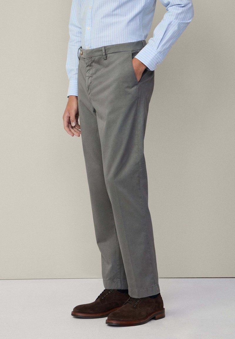 Pantaloni di cotone grigi con tasche frontali, passanti per cintura e taglio dritto. Abbinati a scarpe di suede marroni e una camicia a righe blu chiaro.