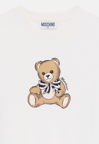 T-shirt en coton blanc avec un ours de dessin animé portant un nœud papillon rayé noir et blanc en sequins, et la marque "Moschino" dans le coin.