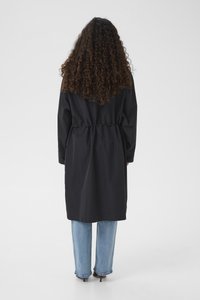 Must veekindel mantel, millel on vööjoon tõmmatud, pikad varrukad ja lahtine lõige, kombineeritud helesiniste laia säärega teksade ja mustade kontsadega.