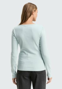 Lang�ärmliges Oberteil aus leicht mintgrünem Rippstoff, mit weitem Halsausschnitt und figurbetontem Design, kombiniert mit dunklen Jeans.