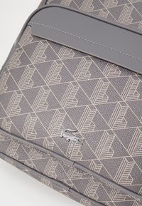 Zaino grigio a motivi con un design geometrico. Esterno testurizzato con dettagli in gomma e un logo di un piccolo coccodrillo.