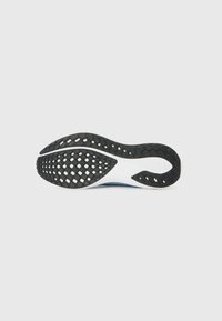 Semelle en caoutchouc noir avec motif de grip texturé ; semelle intermédiaire blanche lisse ; forme incurvée, design flexible, adapté à un usage athlétique.
