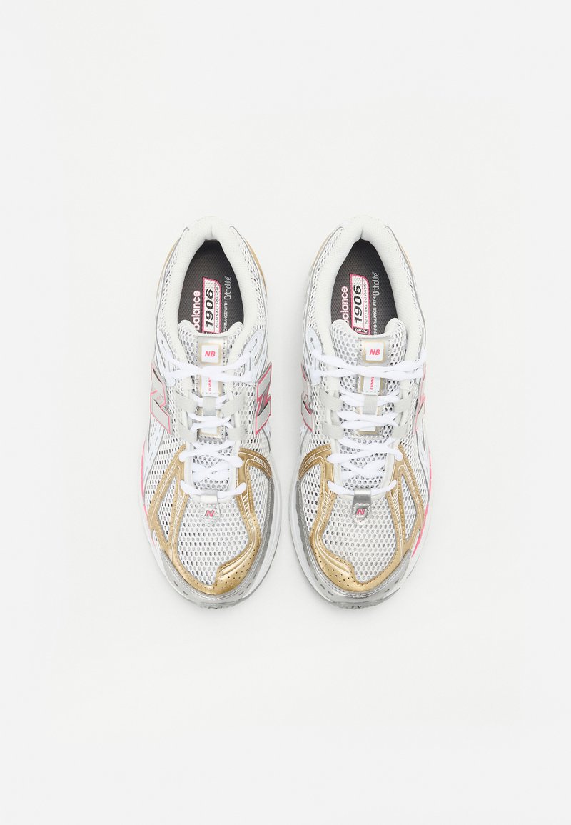 Zapatillas deportivas blancas con parte superior de malla, detalles en rosa y dorado, cuello acolchado y cordones blancos. Diseñadas para ofrecer comodidad y transpirabilidad.