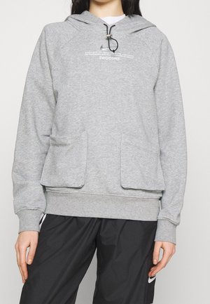 Haut à capuche gris avec un cordon de serrage, poches avant et poignets côtelés. Présente un logo imprimé sur la poitrine. Le tissu semble être un mélange de coton.