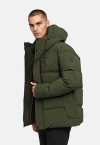 Žalias pūkinis švarkas su gobtuvu, turintis užtrauktuką priekyje, juodus akcentus ir logotipo pleistrą kairiajame petyje. Lygus paviršius ir paminkštintas dizainas.