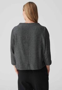 Chaqueta recortada con diseño de espiga en blanco y negro, de mangas three-quarter y cuello redondo, que presenta un diseño limpio y simple.