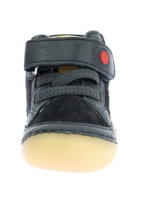 Zapatillas de ante y cuero negro con punta redonda, suela de goma de contraste en color marrón y una correa de velcro con un botón de acento rojo.