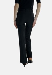 Pantaloni neri su misura con design a gamba dritta, texture liscia e vita con cintura, abbinati a scarpe col tacco nere.