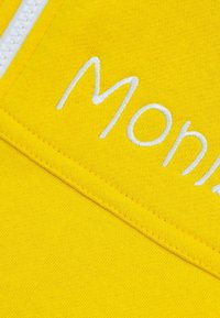 Gelbes Sweatshirtmaterial mit weißem, gesticktem Text "Monr." Hat eine glatte Textur und sichtbare Nähte entlang der Säume.