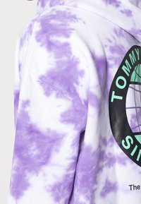 Tie-dye purple hoodie featuring a circular logo with "TOMMY" text. Soft cotton fabric with mixed white background, casual design.
