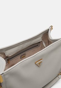 Vaaleanharmaa nahkalaukku, jossa on teksturoitu pinta, kultaiset metalliosat ja sisäinen vetoketjupussi, jossa on logo-detaili sisällä.