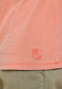 T-shirt corail en coton doux avec une texture subtile. Présente un logo "PULL IN" brodé à l'ourlet et un design à coupe droite.