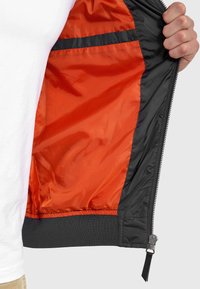 Black bomber jacket with an orange interior lining, featuring a zip front, ribbed cuffs, and waistband, showcasing smooth, lightweight fabric.