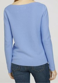 Pull en tricot bleu clair à manches longues, texture côtelée et encolure ronde, associé à un jean bleu foncé avec des détails sur les poches arrière.