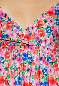 Vestido floral com decote em V, adornado com flores em tons de rosa, vermelho e azul sobre um fundo claro. Tecido texturizado com detalhe de cintura franzida.