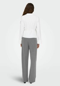 Bijela bluzica dugih rukava s uskim strukom i kragnom, uparena s hlačama širokih nogavica u sivoj boji. Glatka tekstura, ležeran dizajn, bez istaknutih uzoraka.
