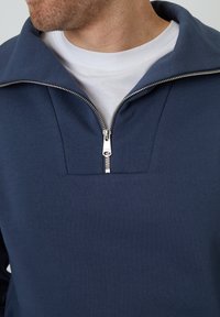 Granatowy sweter z krótkim zamkiem wykonany z miękkiej bawełnianej mieszanki tkanin, z stójką i srebrnym zamkiem błyskawicznym z prostokątnym otwarciem.