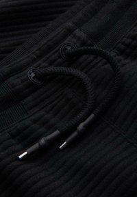 Tessuto nero texturizzato con rigature verticali; presenta un cordoncino con punte nere e due bottoni abbinati.