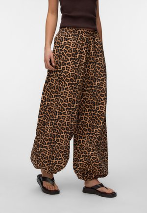 Kobieta w luźnych spodniach w panterkę z elastycznymi ściągaczami, ciemnym topie bez rękawów i czarnych sandałach na platformie z paskiem między palcami.