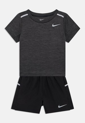 Nike sporta komplekts ar pelēku īsroku kreklu un melnām šortiem. Krekls ir apaļas kakla izgriezuma; abiem gabaliem ir atstarojoši elementi.