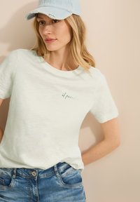 Lichtgroene T-shirt met korte mouwen en een ronde halslijn, voorzien van subtiele turquoise geborduurde tekst "il paradiso" op de borst.