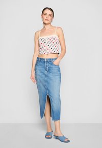 Hvit crop topp med svart og rød tekstmønster, kombinert med et høyhvaist denimskjørt med frontsplitt og frynset kant. Blå sandaler.