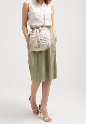 Witte franjes schoudertas van leer, met een trekkoordsluiting en een gladde textuur. Draag met een lichte blouse en een groene rok.
