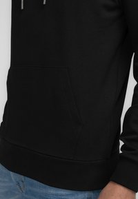 Sudadera negra con bolsillo canguro, dobladillo acanalado y puños. Fabricada en un tejido suave con una textura lisa y detalles de diseño mínimos.