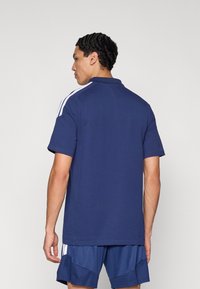 Μπλε σκούρο πόλο μπλουζάκι με κοντά μανίκια και γιακά στο πίσω μέρος. Διαθέτει λευκές ρίγες στους ώμους. Το ύφασμα φαίνεται μαλακό και λείο.