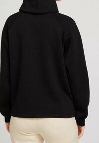 Černá mikina s vysokým límcem, raglánovými rukávy a žebrovanými manžetami. Měkká textura, minimalistický design a žádné viditelné grafiky nebo vzory.