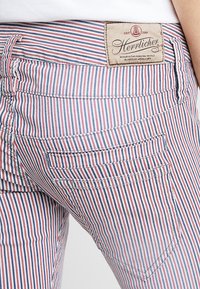 Randiga tygbyxor med vertikala röd, vit och blå ränder, med en rektangulär lapp bak och två bakfickor.