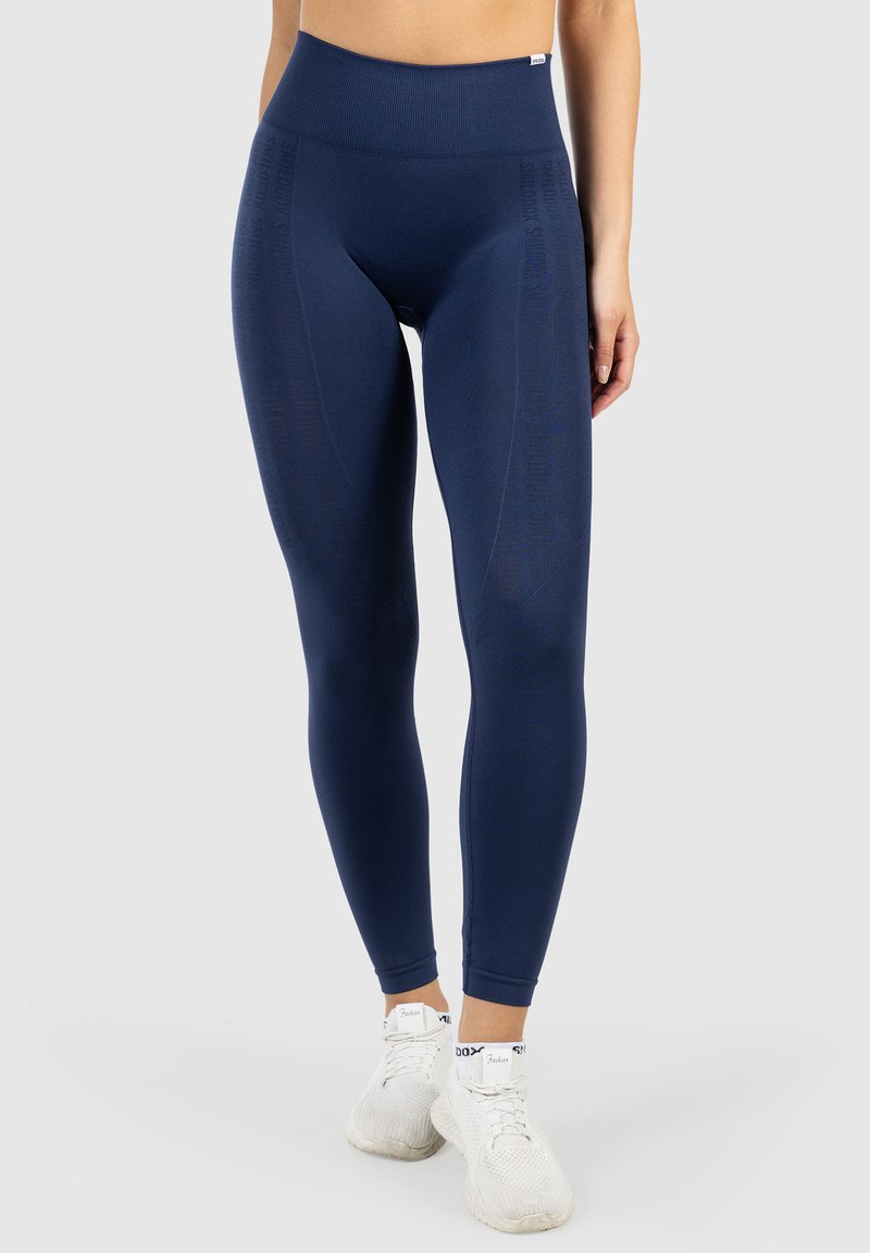 Marina leggings med hög midja, tillverkade av ett deformerbart och slätt material. Har en vertikal textdesign på sidorna för extra detalj.