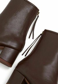 Brown leather ankle boots with a smooth texture, featuring a block heel and side zippers with tassels for easy access.