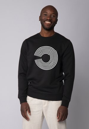 Sweatshirt noir avec un graphique de cercles concentriques blancs. Il possède des manches longues et un col rond. Tissu lisse, coupe décontractée.