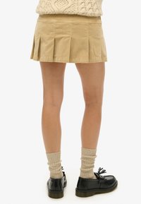 Beige plisseret nederdel lavet af bomuldsblanding, med flere plisseringer, en flad talje, og kombineret med sorte sko og ribbet beige strømper.