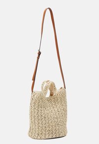 Borsa a secchiello in paglia intrecciata beige con manici corti e tracolla in pelle marrone regolabile su sfondo bianco.