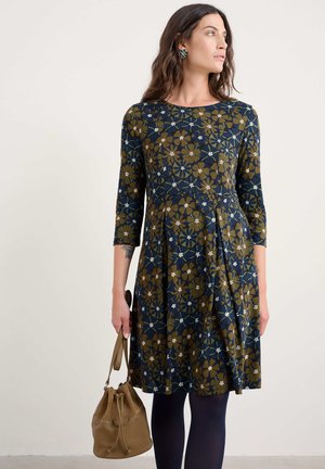Robe à motif floral avec manches trois-quarts, en marine et vert olive, avec des fleurs blanches. Assortie à un sac seau marron.