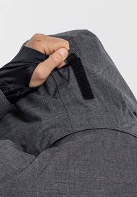 Gray fabric jacket with a textured finish. Close-up of a hand gripping a black Velcro strap near a seam.
