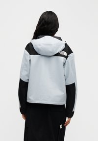 Ελαφριά μπλε και μαύρη μπεζονέτα μπουφάν με κουκούλα, με λογότυπο στην πλάτη και υφασμάτινη υφή, σχεδιασμένη για υπαίθριες δραστηριότητες.