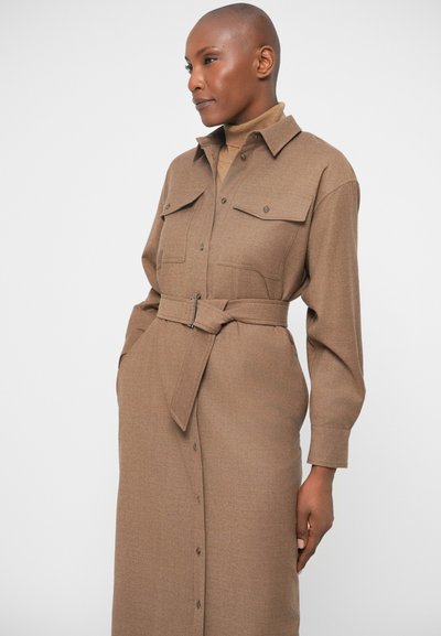 Vestido castanho de botão, feito de tecido texturizado, com dois bolsos no peito, mangas longas e uma cintura cingida com cinto para um formato elegante.