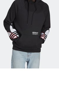Svart hoodie med framfickor, har vita och röda accentremsor på ärmarna och en Adidas-logotyp på bröstet. Tillverkad av mjukt material.