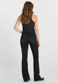 Zwarte flare jeans met een hoge taille, voorzien van achterzakken en een gladde textuur. Gedragen met een zwart tanktop en platte schoenen.