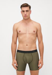 Boxer da uomo verde oliva realizzati in materiale elasticizzato con un design aderente. Vita nera con la scritta "ARMOUR" in un carattere in grassetto.