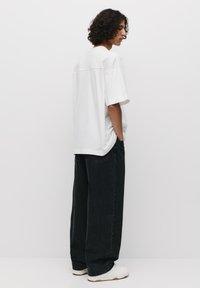 Witte oversized t-shirt met korte mouwen, gecombineerd met losse zwarte jeans en witte sneakers, getoond vanuit de zijkant en van achteren.
