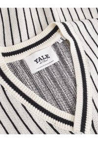 Krém és fekete csíkos pulóver V-nyakkal. Szélesített gallér és texturált minta jellemzi. A címke „Yale” felirattal és szőtt dizájnnal készült.