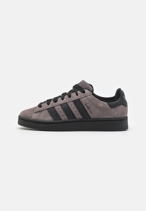 Szara zamszowa tenisówka Adidas Campus z czarnymi paskami, czarnymi sznurówkami i czarną podeszwą, pokazana z wewnętrznego profilu bocznego.